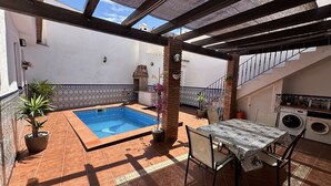 Un patio con piscina, una mesa con sillas, un horno de ladrillo y zona de lavandería.