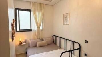 Um quarto com uma cama, um candelabro, uma janela com cortinas e uma mesa de cabeceira.