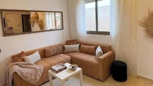 A living room with a beige sofa, a white coffee table, and a black ottoman.