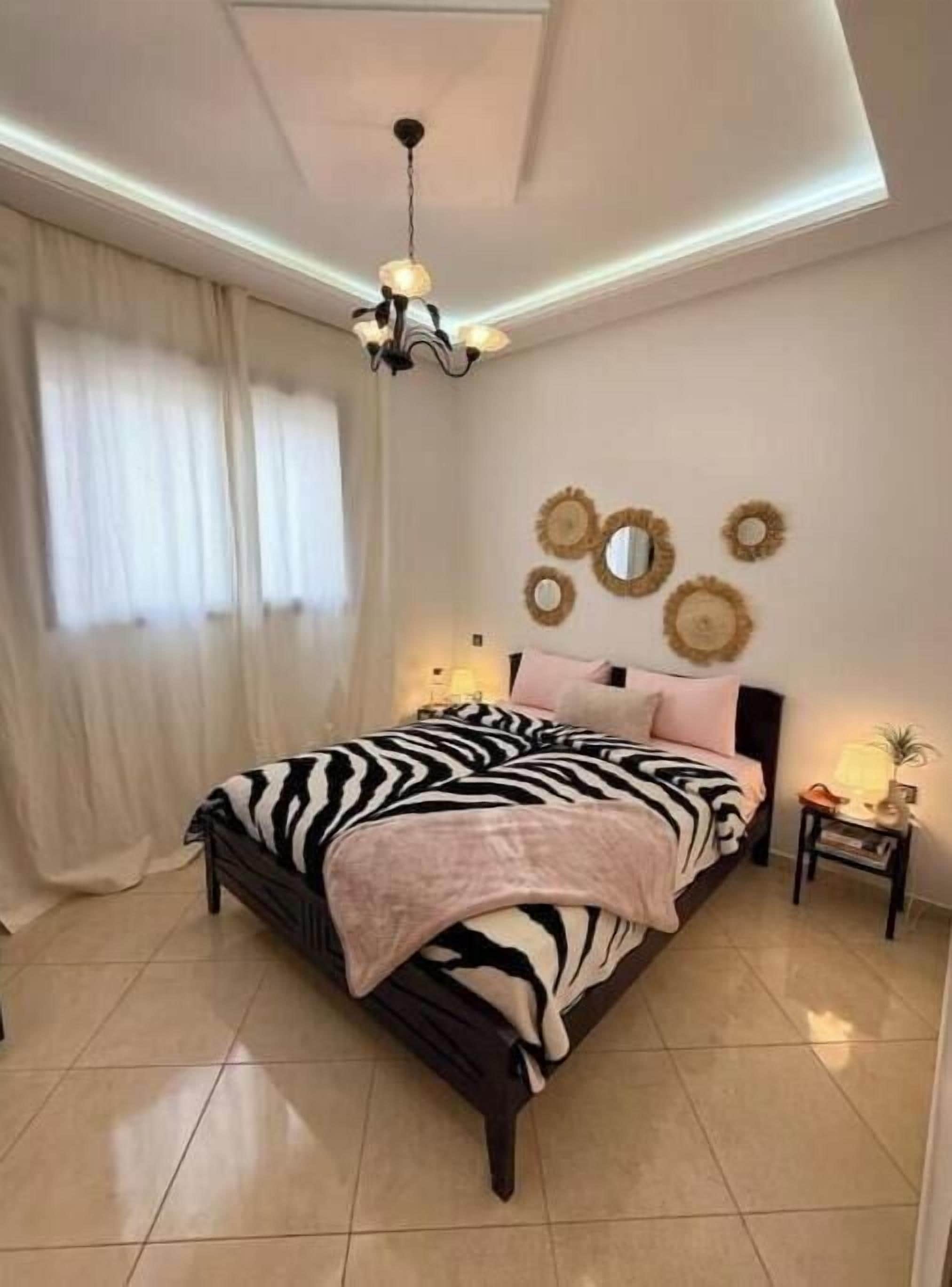 Ein Schlafzimmer mit Bett, Vorhängen, einer Pendelleuchte, Wanddekoration und einem Nachttisch.