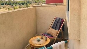 Un petit balcon avec une table ronde, deux chaises et un fauteuil suspendu.
