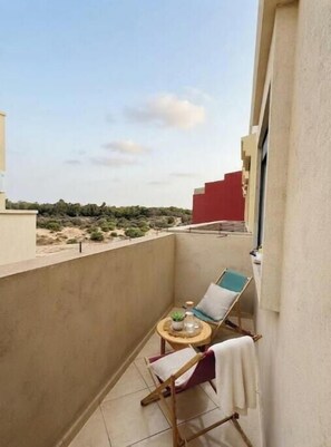 A balcony with a chair, a small table, and a view of the landscape. - A Modern and Elegant Setting • Forest View • Near the Beach (Essaouira)
