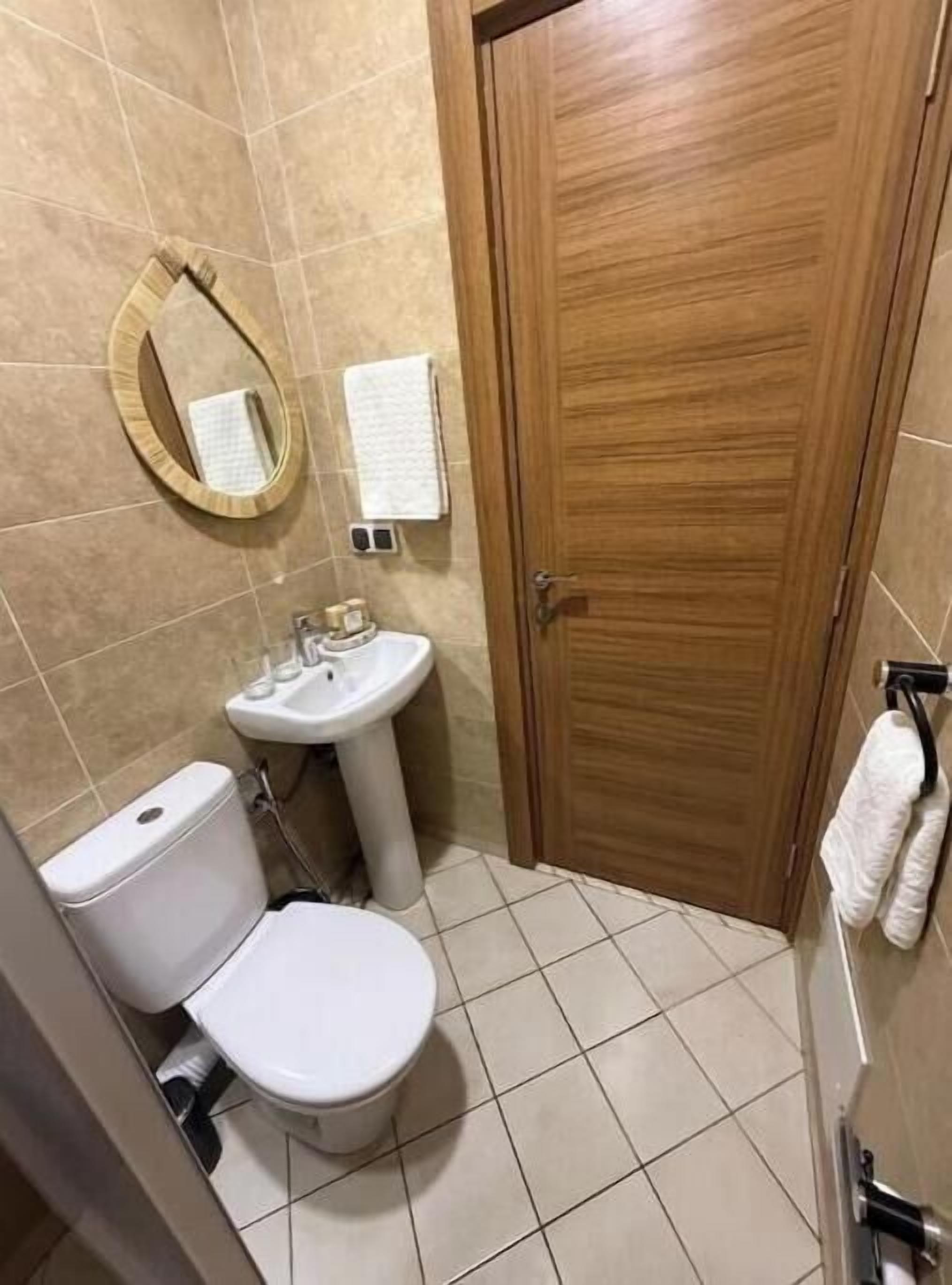 Baño con inodoro, lavamanos, espejo y puerta de madera.