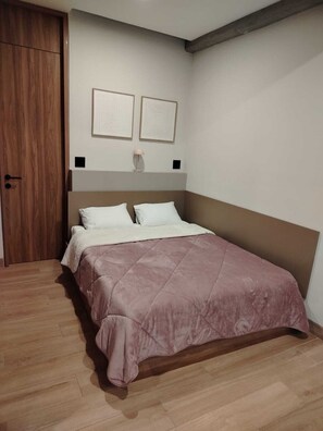 Ein Schlafzimmer mit einem Bett, Holzboden, einer Tür und zwei an der Wand befestigten Bildern.