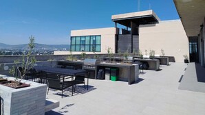 A rooftop patio with outdoor furniture, a grill, and a view of the cityscape. - Margot Premier Apartment (Guadalajara)