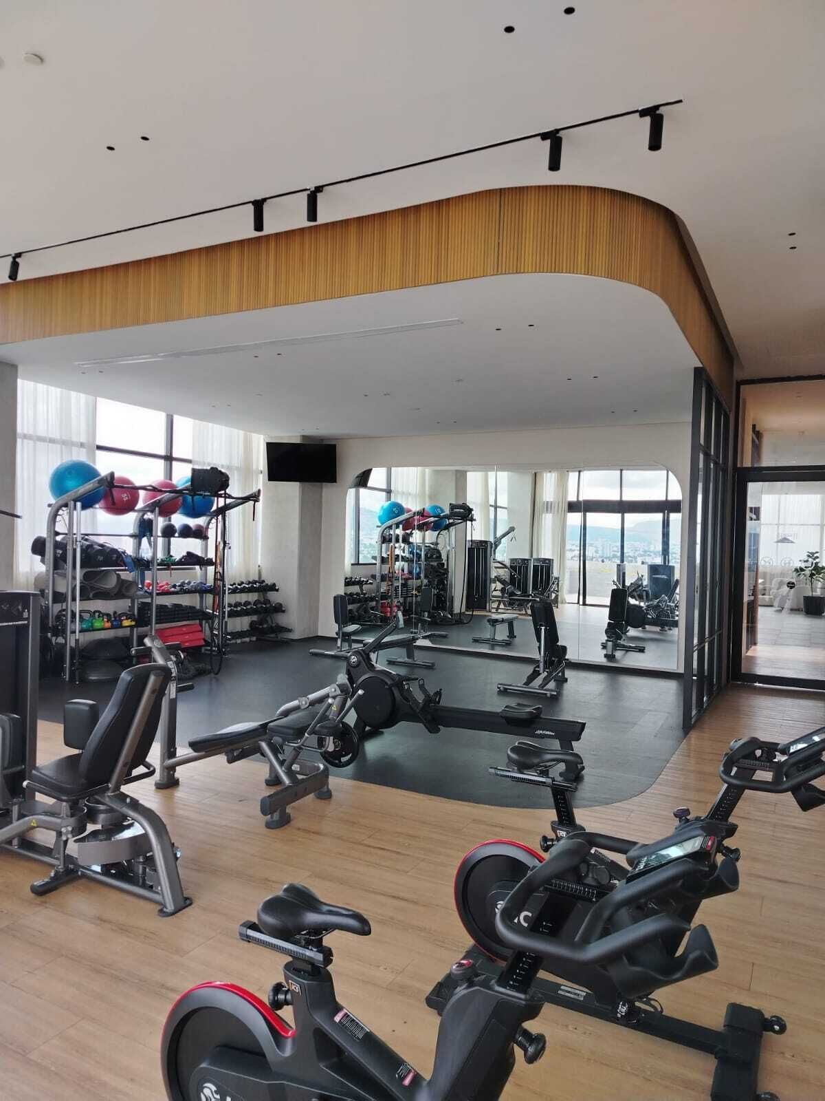 A gym with cardio machines, weightlifting equipment, and a large mirror reflecting the space.