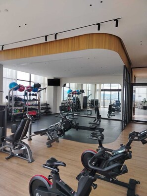 Ein Fitnessstudio mit Cardiogeräten, Gewichten und einem großen Spiegel, der den Raum reflektiert.