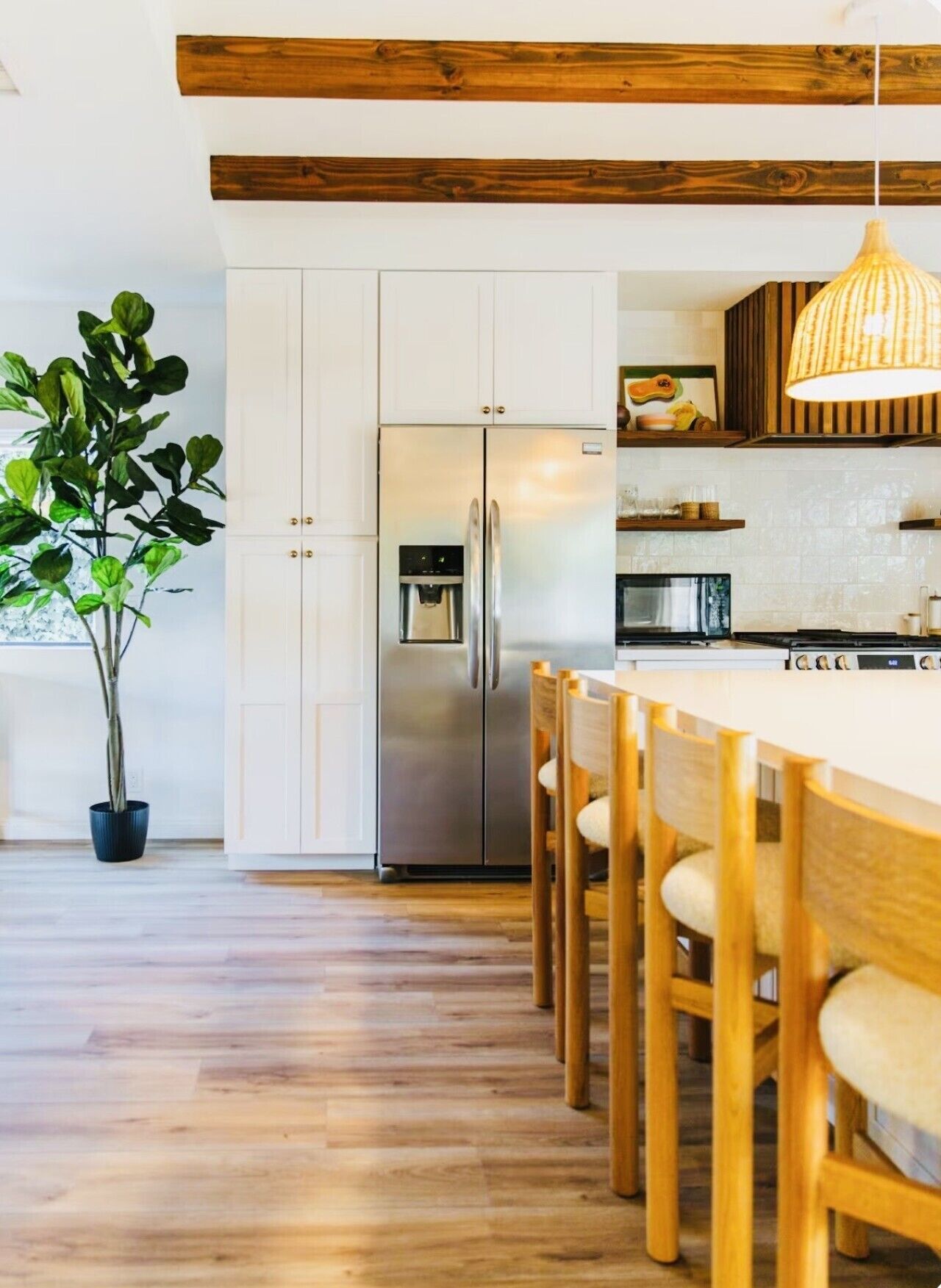 Une cuisine moderne avec des meubles blancs, un réfrigérateur en acier inoxydable, une table à manger en bois et des chaises.
