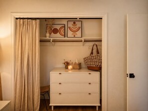 A room with a white dresser, a shelf with decorative items, a hanging bag, and a curtain. - Stylish Designer Home Near Downtown & Bike Path (Ojai)