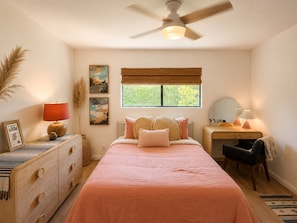 Un dormitorio con cama, escritorio, silla, ventilador de techo y ventana con persianas.