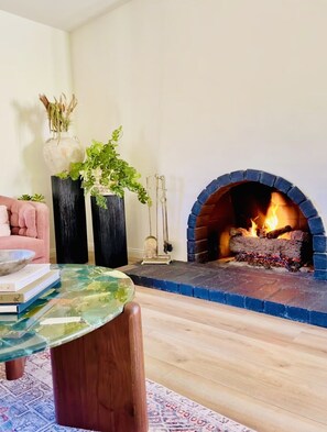A living room with a stone fireplace, a glass coffee table, and a pink sofa. - Stylish Designer Home Near Downtown & Bike Path (Ojai)