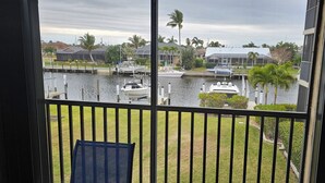 Une vue depuis un balcon donnant sur une marina où sont amarrés des bateaux, avec une zone herbeuse et des immeubles d’habitation en arrière-plan.