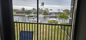 Blick von einem Balkon auf einen Hafen mit vertäuten Booten, eine Rasenfläche und Wohnhäuser im Hintergrund.