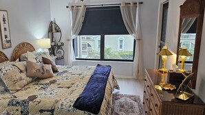 Une chambre à coucher comprenant un lit, une table de chevet, une lampe, une fenêtre avec des rideaux et une étagère fixée au mur.