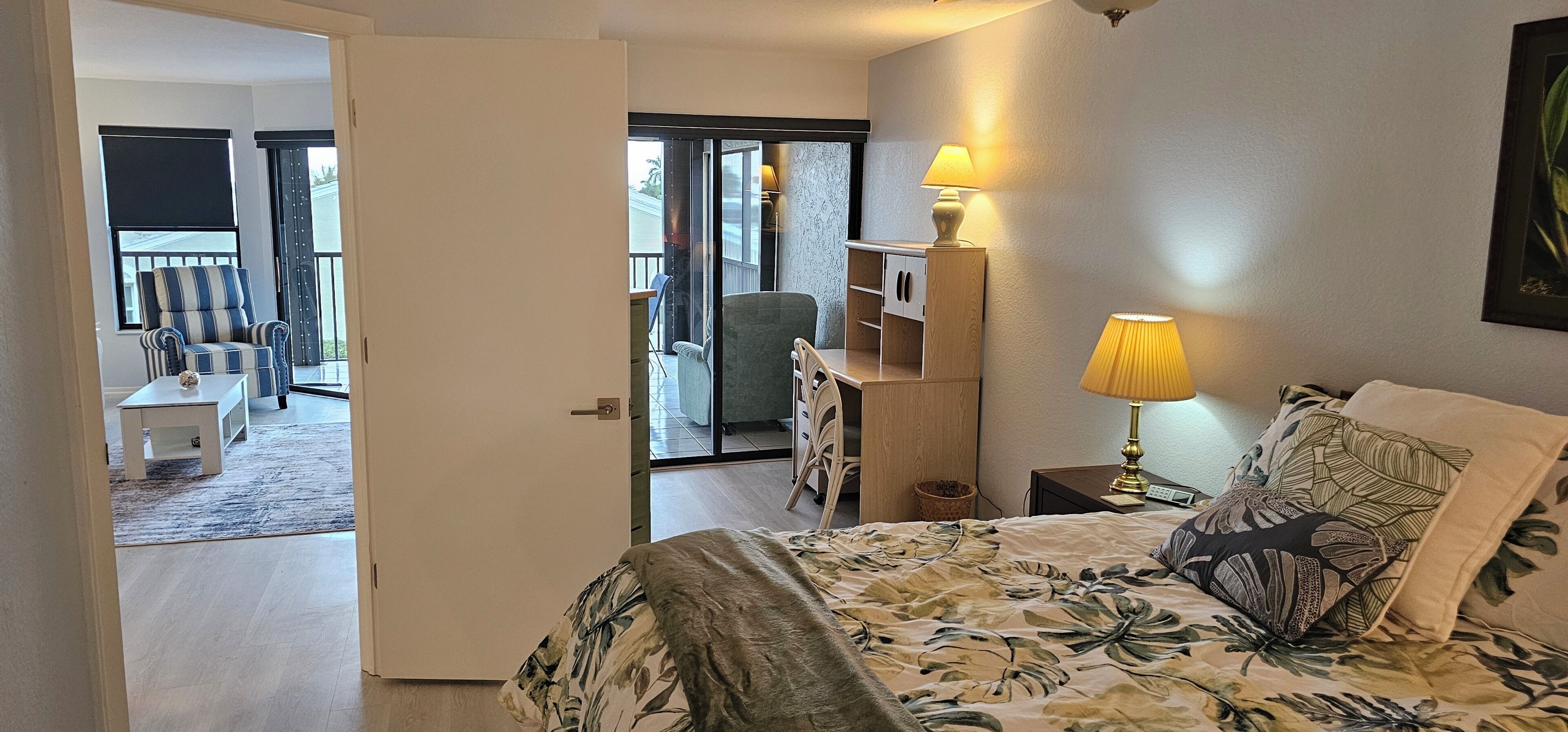 Ein Hotelzimmer mit Bett, Nachttisch, Lampe, Stuhl und Blick auf den Balkon.
