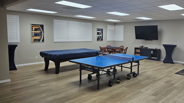 Une pièce équipée d’une table de ping-pong, d’un jeu de fléchettes et d’un téléviseur fixé au mur.