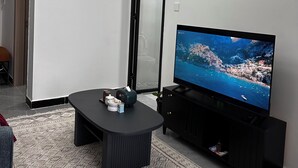 Ein modernes Wohnzimmer mit Fernseher, einem schwarzen Couchtisch und einem gemusterten Teppich.