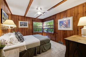 Ein Schlafzimmer mit einem Bett, einem Deckenventilator, Holzwänden, einem Fenster mit Jalousien und einem Bild an der Wand.