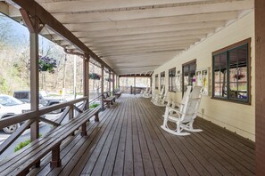 Eine überdachte Veranda mit hölzernen Bänken und Schaukelstühlen, einem Holzboden und bepflanzten Blumenkörben.