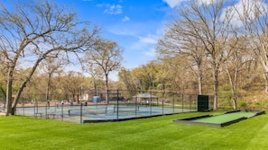 Ein gepflegter Park mit Tennisplatz, Laube und einer Grünfläche.