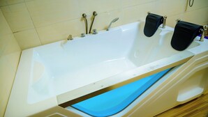 Una bañera blanca con interior azul, grifería cromada y piso de madera.