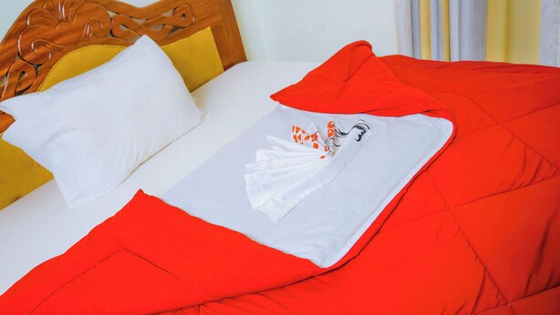 Una cama con un edredón rojo, una almohada blanca y una colcha blanca con diseños anaranjados y negros.