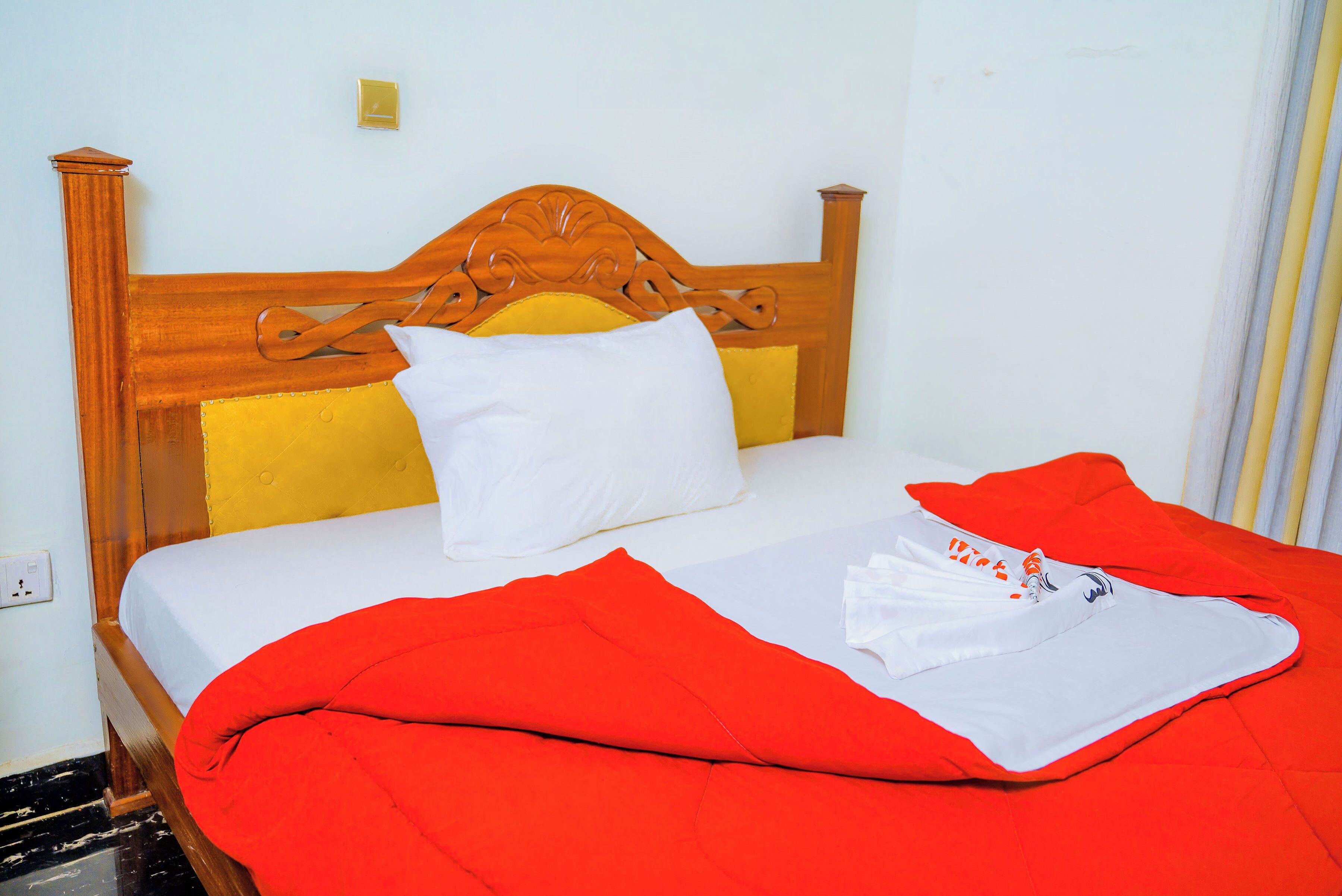 Un lit avec une tête de lit en bois, du linge de lit blanc et une couverture rouge.