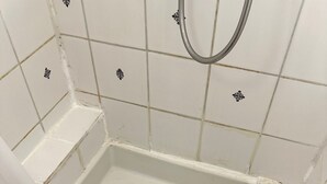 Ein Badezimmer mit weißen Fliesen, einer Duschkabine und einem roten Handtuch auf dem Boden.