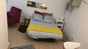 Ein kleines, gemütliches Schlafzimmer mit Bett, Nachttisch, Stuhl, Schreibtisch und Spiegel.