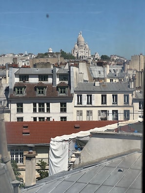 A cityscape with a prominent historical building in the background, surrounded by residential buildings with varied roof styles. - Studio apartment in the heart of Paris with a view of Sacré-Cœur (Paris)