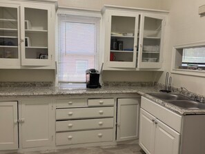 A kitchen with white cabinets, a granite countertop, a coffee maker, and a window with blinds. - Fantastic 3-bedroom house with AC in charming Benson Omaha (Omaha)