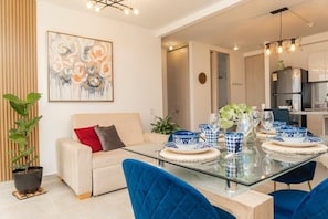 Ein modernes Wohnzimmer mit einem Glastisch für vier Personen, einer Couch, einem Blumentopf und einem zeitgenössischen Gemälde.