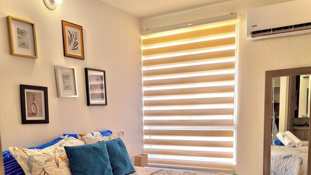 A bedroom with a bed, framed pictures on the wall, a window with blinds, and an air conditioning unit. - Escape to Cartagena and relax at Azul Sereno (Bolivar)