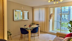 A dining area with a glass table, chairs, a mirror, and a view of a residential building through a sliding glass door. - Escape to Cartagena and relax at Azul Sereno (Bolivar)