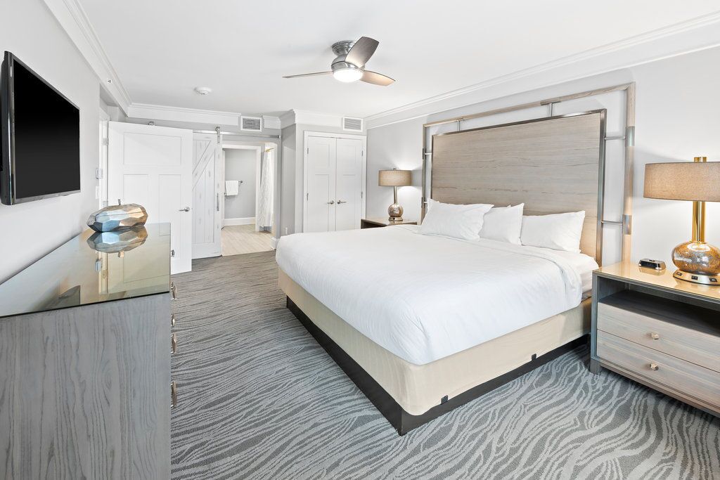 Ein Hotelzimmer mit Bett, Nachttischen, Fernseher, Deckenventilator und einer Tür zu einem Badezimmer.