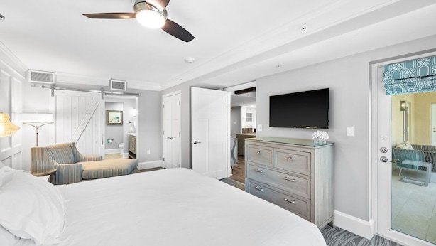 A hotel room with a large bed, a flat-screen TV mounted on the wall, a dresser, and a ceiling fan.