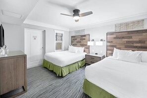 A hotel room with two beds, a ceiling fan, a wooden headboard, a nightstand, and a desk with a lamp. - Spacious 4BR Villa Near Beach & Access to Pools (Cape Canaveral)