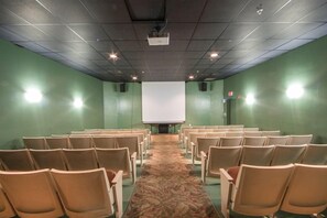Ein Konferenzraum mit Stuhlreihen, die auf eine leere Projektionsleinwand zeigen, grünen Wänden und einem Teppichboden.