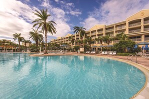 A hotel with a large pool, palm trees, and a clear sky. - Spacious 4BR Villa Near Beach & Access to Pools (Cape Canaveral)