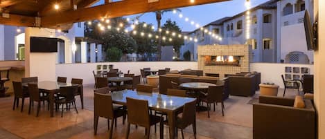 Eine Terrasse im Freien mit Tischen und Stühlen, einem Kamin aus Ziegelsteinen und Lichterketten.