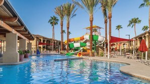 Una piscina con tobogán de agua, palmeras y zonas de estar al aire libre.