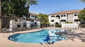 A swimming pool with lounge chairs and a pergola, surrounded by a building with arched windows and a tiled roof.