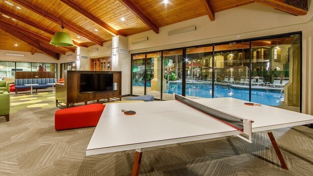 Un espace piscine intérieur moderne, équipé d’une table de ping-pong, de sièges et d’un téléviseur.