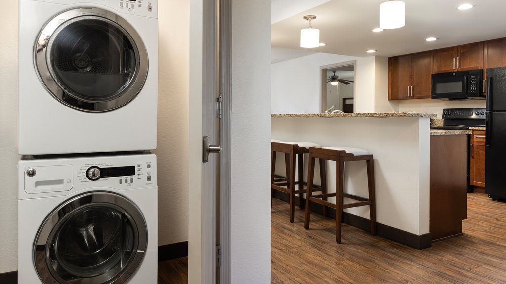 A laundry room with stacked washers and dryers, a kitchen with wooden cabinets, granite countertops, and a bar area.