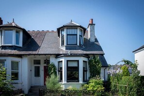 Una casa de estilo victoriano con ventanal saliente, puerta roja y fachada blanca.