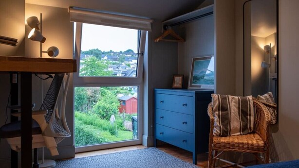 Ein Schlafzimmer mit großem Fenster, Schreibtisch, Stuhl und einer Garderobe.