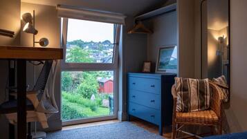 A bedroom with a large window, a desk, a chair, and a hanging coat rack.