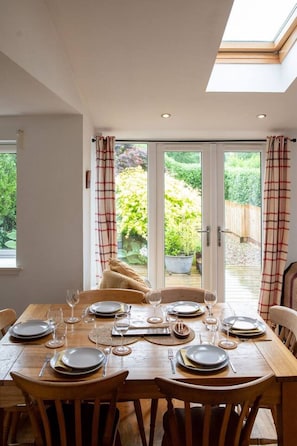 A dining room with a table set for six, large windows with curtains, and a view of a garden.