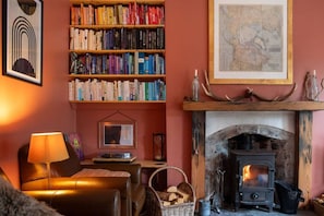 A cozy living room with a fireplace, a bookshelf filled with books, a framed picture on the wall, and a lamp.