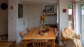 A dining area with a wooden table, chairs, a vase with sunflowers, and a framed picture on the wall.